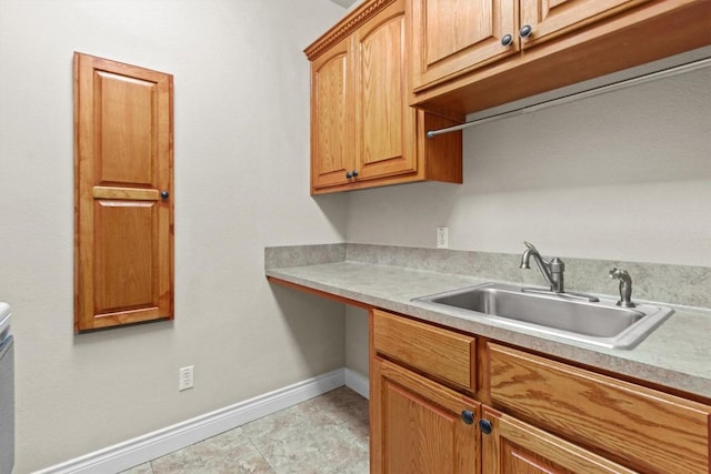 kitchen featuring brown cabinets, light countertops, a sink, and baseboards