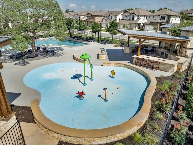 community pool with outdoor dry bar, a patio area, a water play area, fence, and a residential view