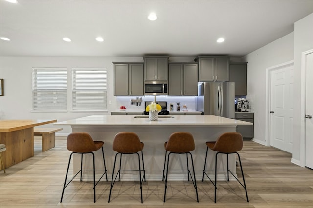 kitchen featuring a center island with sink, appliances with stainless steel finishes, a kitchen breakfast bar, light countertops, and gray cabinetry