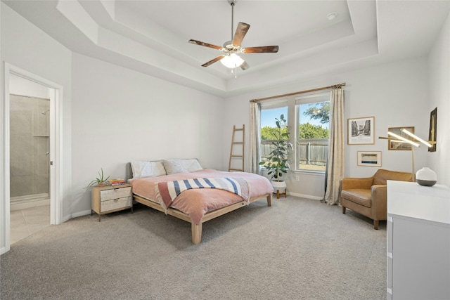 bedroom featuring baseboards, light colored carpet, ensuite bath, ceiling fan, and a tray ceiling