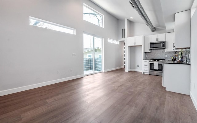 kitchen featuring high vaulted ceiling, stainless steel appliances, white cabinets, dark countertops, and tasteful backsplash