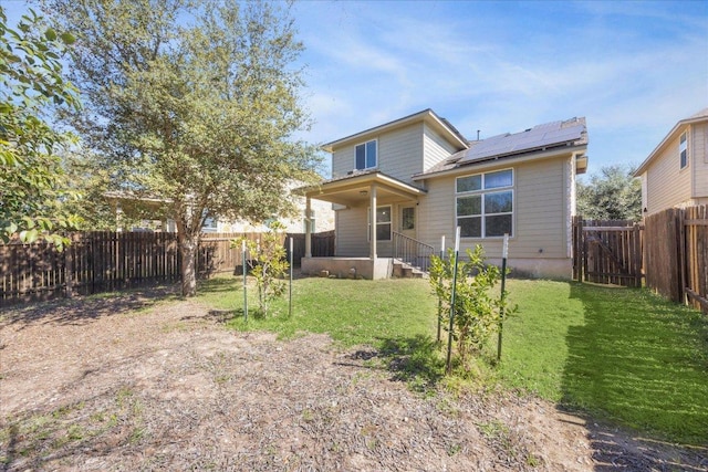 rear view of house featuring a fenced backyard, roof mounted solar panels, and a lawn