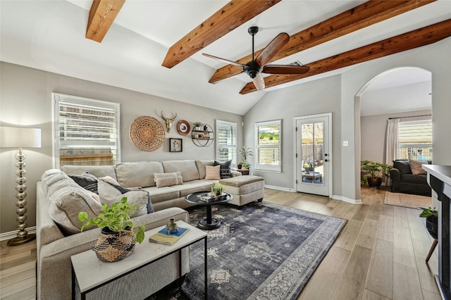 living room with light wood finished floors, baseboards, arched walkways, lofted ceiling with beams, and ceiling fan