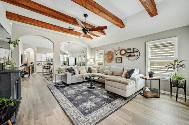 living area featuring arched walkways, visible vents, light wood-style flooring, lofted ceiling with beams, and a ceiling fan