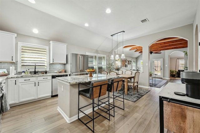 kitchen featuring a kitchen island, light stone counters, hanging light fixtures, stainless steel appliances, and white cabinetry