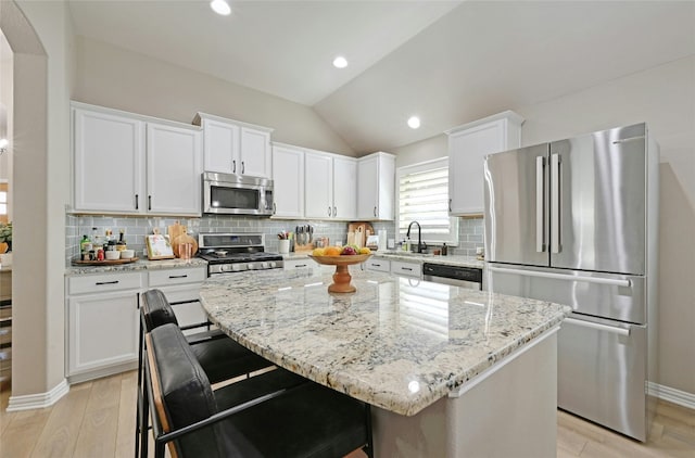 kitchen with white cabinets, lofted ceiling, a kitchen island, appliances with stainless steel finishes, and light stone countertops