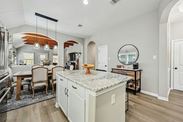 kitchen with visible vents, white cabinets, a kitchen island, light stone countertops, and pendant lighting