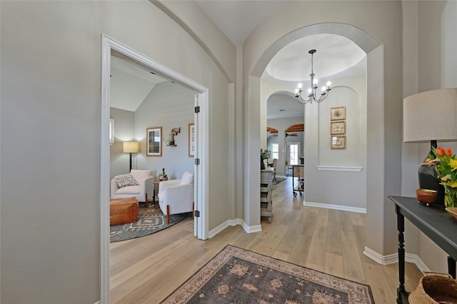 hallway featuring arched walkways, a notable chandelier, light wood-style flooring, and baseboards