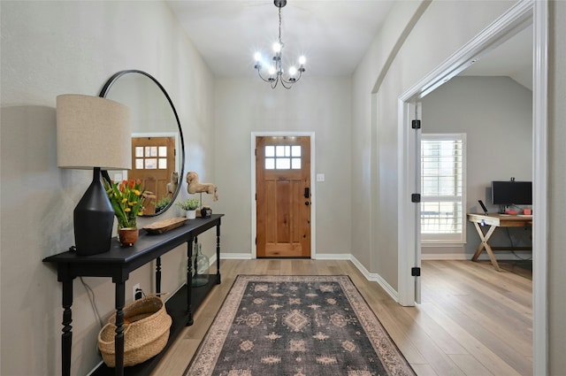 entrance foyer featuring light wood-style floors, vaulted ceiling, baseboards, and an inviting chandelier