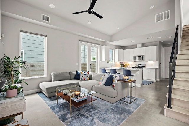 living room with ceiling fan, visible vents, concrete flooring, and stairway