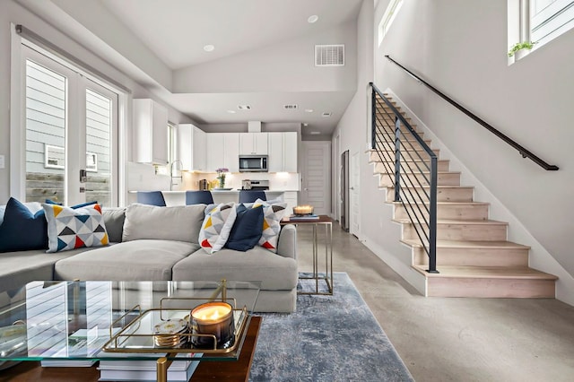 living area featuring a healthy amount of sunlight, high vaulted ceiling, stairs, and visible vents