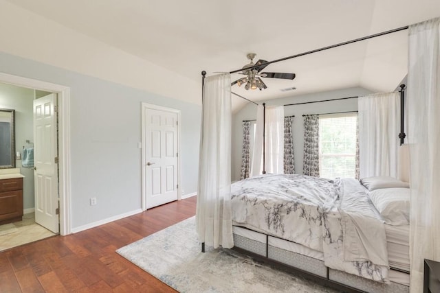 bedroom featuring visible vents, baseboards, lofted ceiling, wood finished floors, and ensuite bathroom