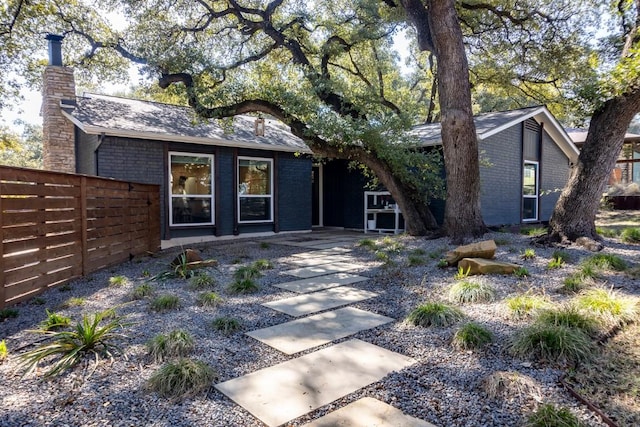 view of front of home with a chimney, fence, a patio, and brick siding