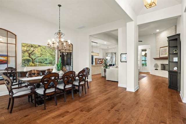 dining area with visible vents, baseboards, wood finished floors, a brick fireplace, and a notable chandelier