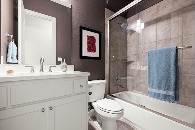 bathroom featuring toilet, a textured wall, enclosed tub / shower combo, and vanity