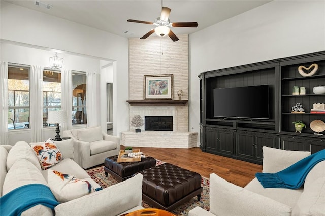 living area featuring a brick fireplace, ceiling fan, visible vents, and wood finished floors