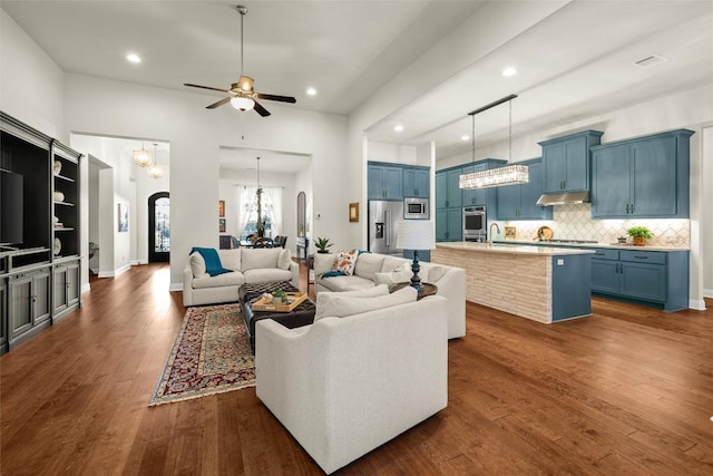 living area featuring arched walkways, dark wood-style flooring, ceiling fan with notable chandelier, and recessed lighting