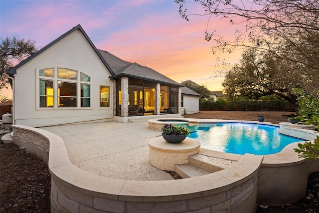 pool at dusk featuring a patio area and a pool with connected hot tub