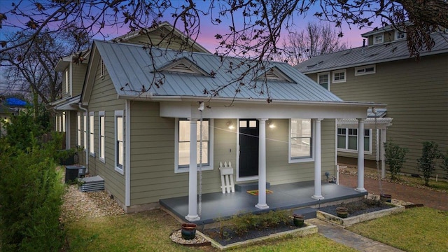 view of front of home with covered porch, metal roof, a lawn, and cooling unit