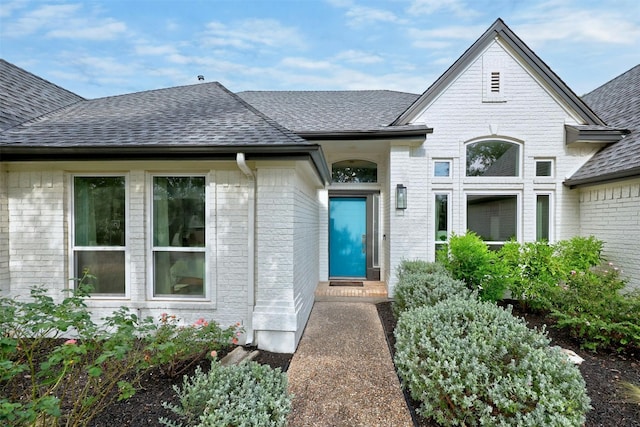 entrance to property featuring roof with shingles and brick siding