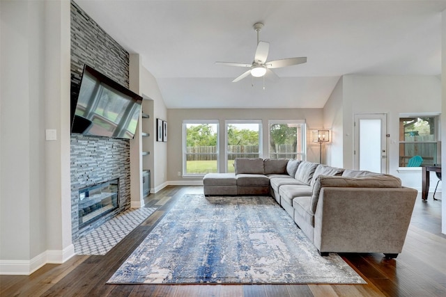 living room featuring lofted ceiling, a stone fireplace, a ceiling fan, baseboards, and dark wood-style floors