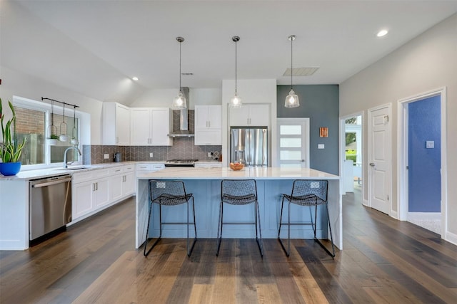 kitchen featuring light countertops, appliances with stainless steel finishes, white cabinetry, a kitchen island, and wall chimney exhaust hood