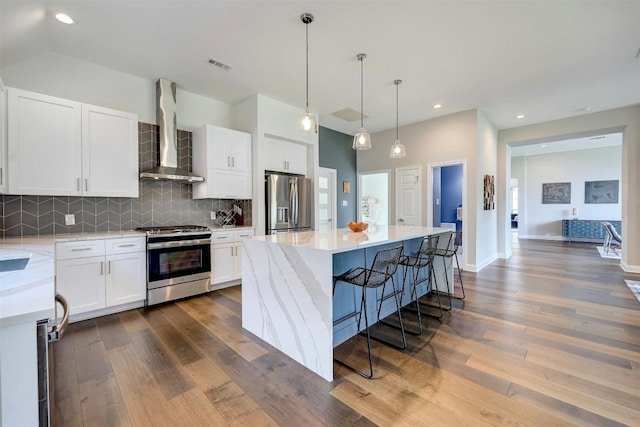 kitchen with appliances with stainless steel finishes, white cabinetry, a kitchen island, and wall chimney exhaust hood