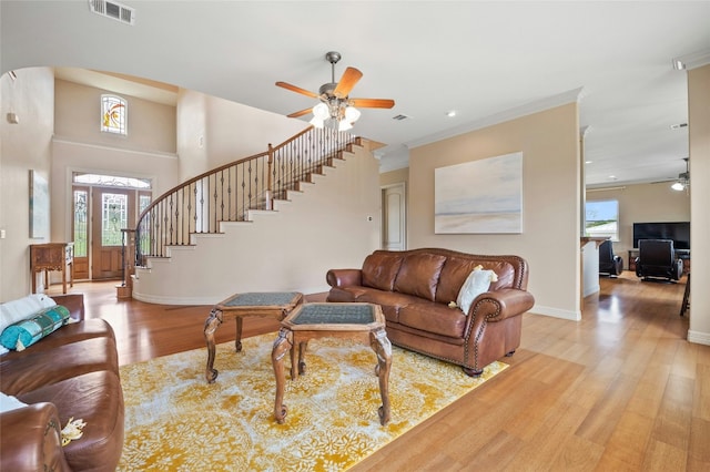 living area with visible vents, baseboards, light wood-style flooring, ceiling fan, and stairs