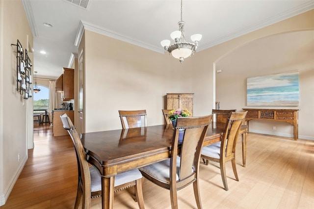 dining room featuring arched walkways, a chandelier, baseboards, light wood finished floors, and crown molding