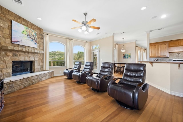 living area with a fireplace, visible vents, ornamental molding, a ceiling fan, and light wood-type flooring