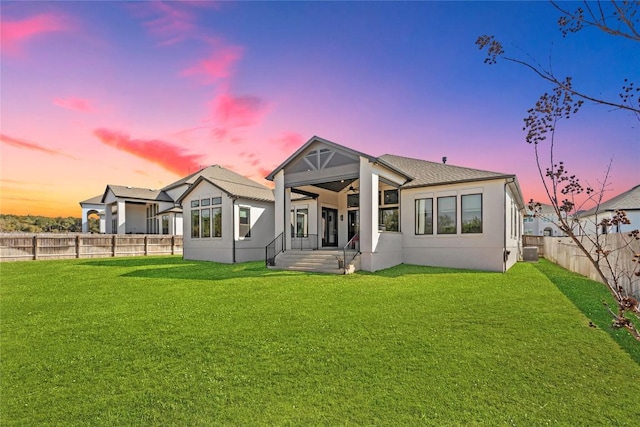 back of property at dusk featuring a fenced backyard, central AC, a lawn, and stucco siding