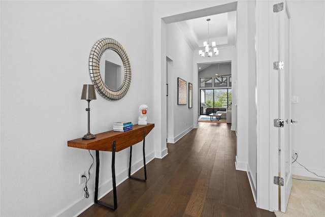 corridor featuring a notable chandelier, a tray ceiling, wood finished floors, and baseboards