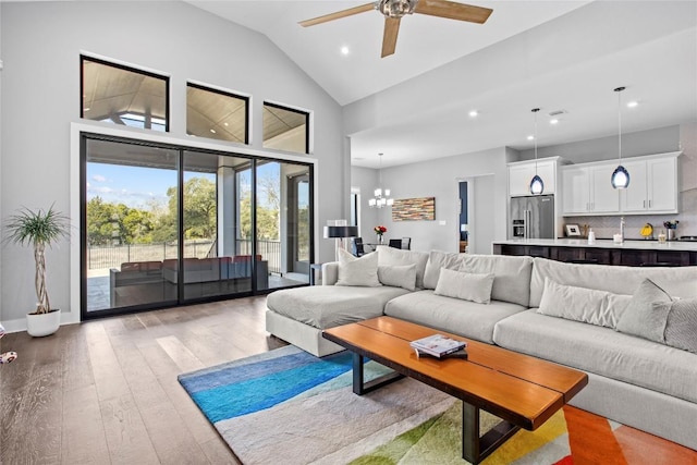 living area featuring recessed lighting, high vaulted ceiling, light wood-type flooring, baseboards, and ceiling fan with notable chandelier