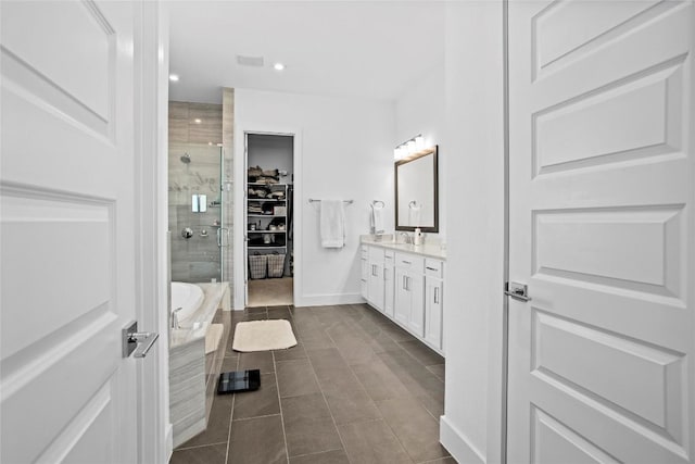 bathroom featuring a walk in closet, a garden tub, a stall shower, vanity, and baseboards