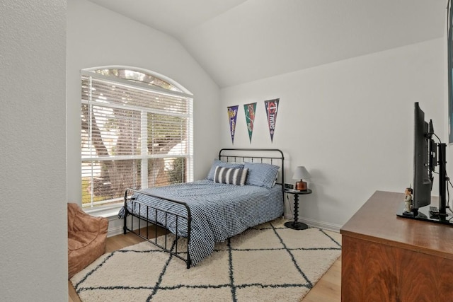 bedroom featuring light wood-type flooring, baseboards, and vaulted ceiling