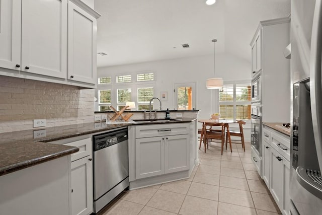 kitchen featuring stainless steel appliances, a sink, white cabinets, dark stone countertops, and pendant lighting