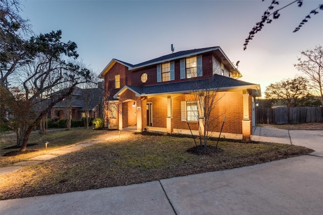 traditional-style home with covered porch, brick siding, a front yard, and fence