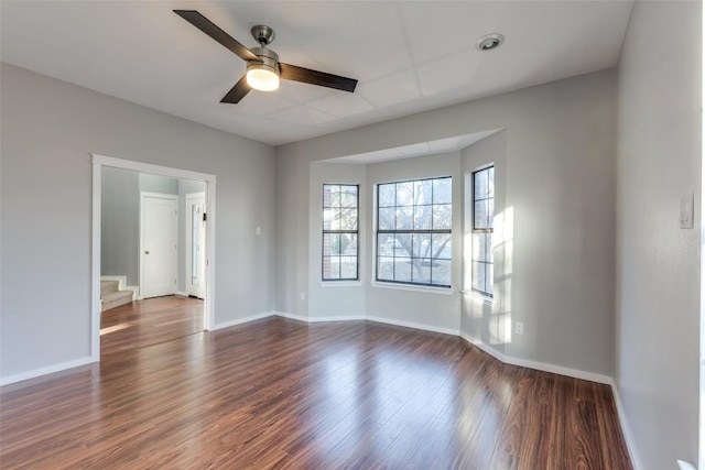 spare room with stairs, a ceiling fan, dark wood-style flooring, and baseboards