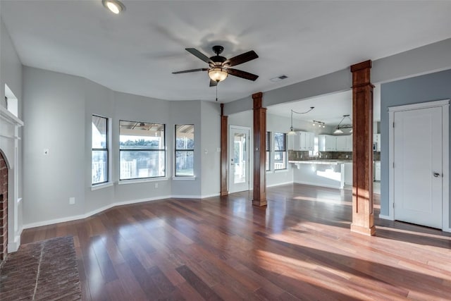 unfurnished living room featuring a fireplace, visible vents, a ceiling fan, dark wood finished floors, and ornate columns