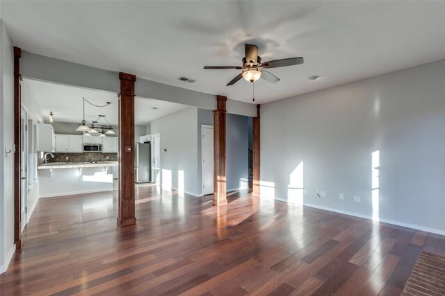 empty room featuring visible vents, dark wood-type flooring, a sink, ceiling fan, and ornate columns