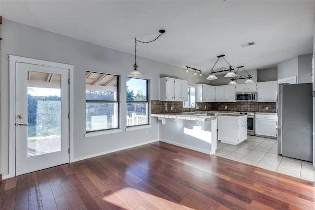 kitchen with light countertops, backsplash, appliances with stainless steel finishes, white cabinets, and a sink