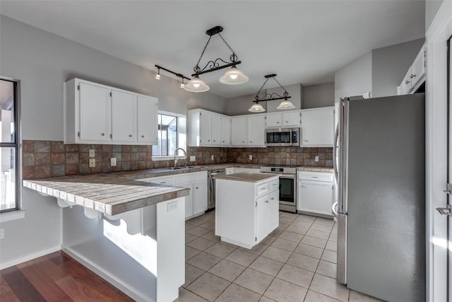 kitchen with decorative light fixtures, backsplash, appliances with stainless steel finishes, white cabinets, and a peninsula