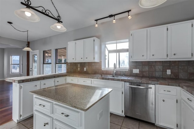 kitchen featuring a sink, backsplash, stainless steel dishwasher, white cabinetry, and a peninsula