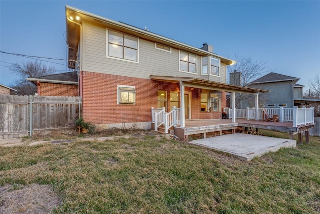 rear view of property featuring brick siding, a chimney, a lawn, fence, and a deck