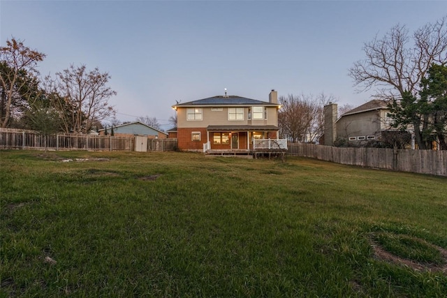 rear view of property featuring a yard, a fenced backyard, a chimney, and a wooden deck