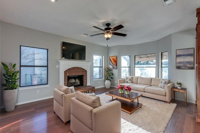 living room with a brick fireplace, a ceiling fan, dark wood-style flooring, and baseboards