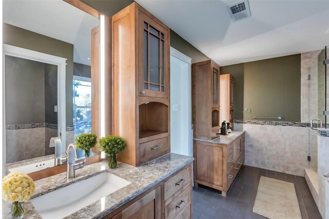 bathroom featuring visible vents, a shower stall, two vanities, tile walls, and a sink