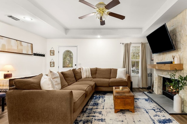living room featuring wood finished floors, a ceiling fan, visible vents, a high end fireplace, and a tray ceiling