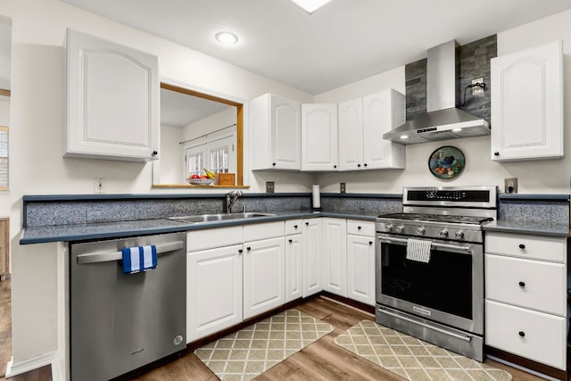 kitchen with stainless steel appliances, white cabinetry, a sink, and wall chimney range hood