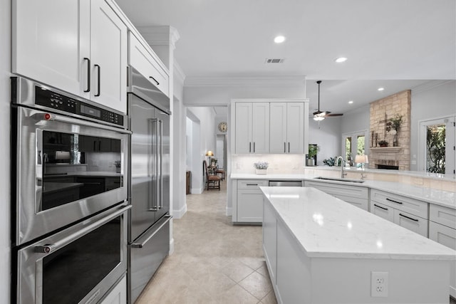 kitchen featuring appliances with stainless steel finishes, ornamental molding, white cabinets, a sink, and a kitchen island